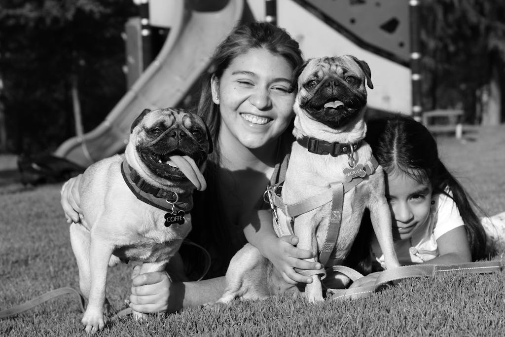 Family enjoying a sunny day outdoors with two happy pugs. Black and white photo.